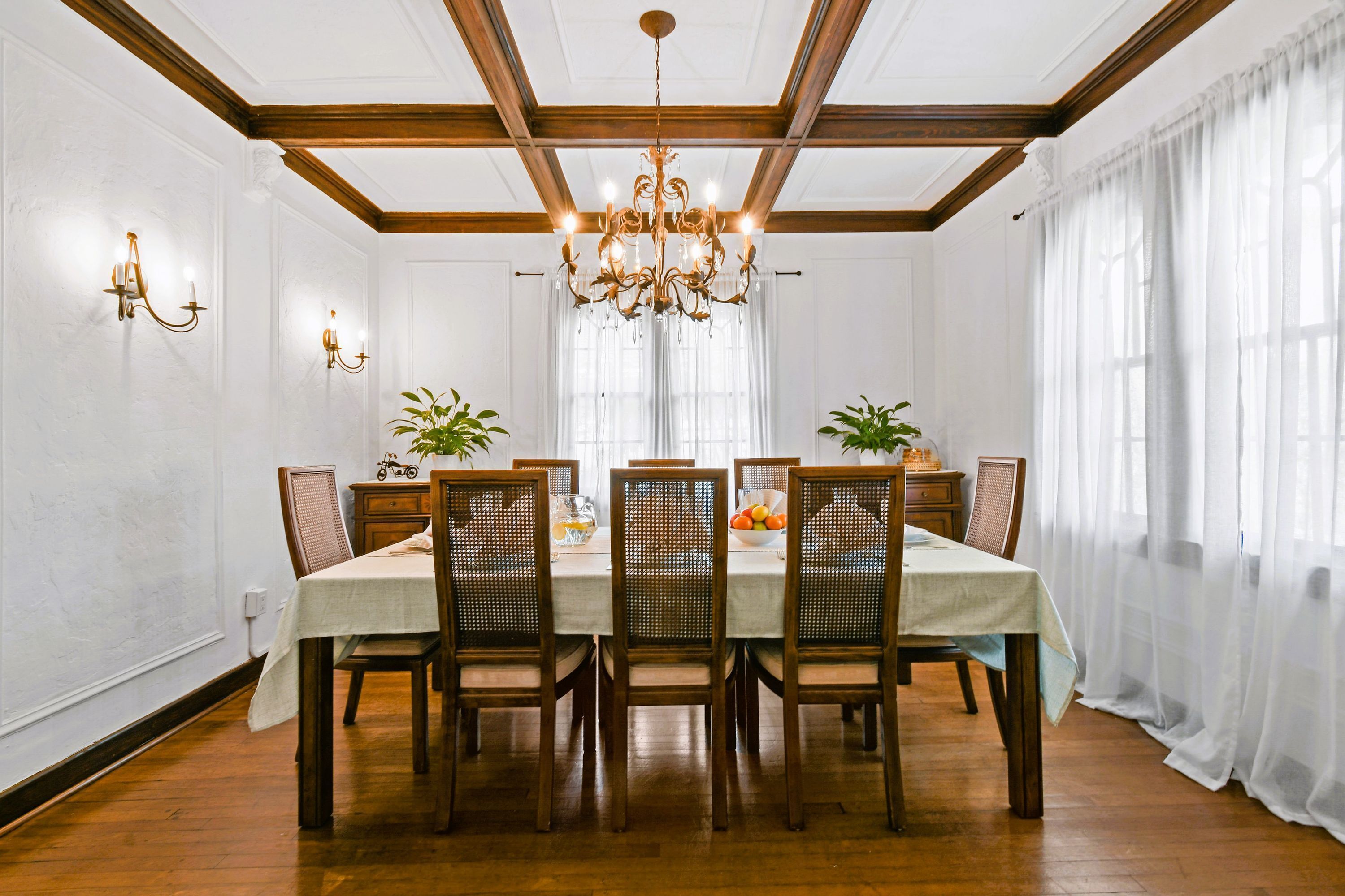 Comedor con mesa de madera, sillas, candelabro y ventana con cortinas translúcidas.