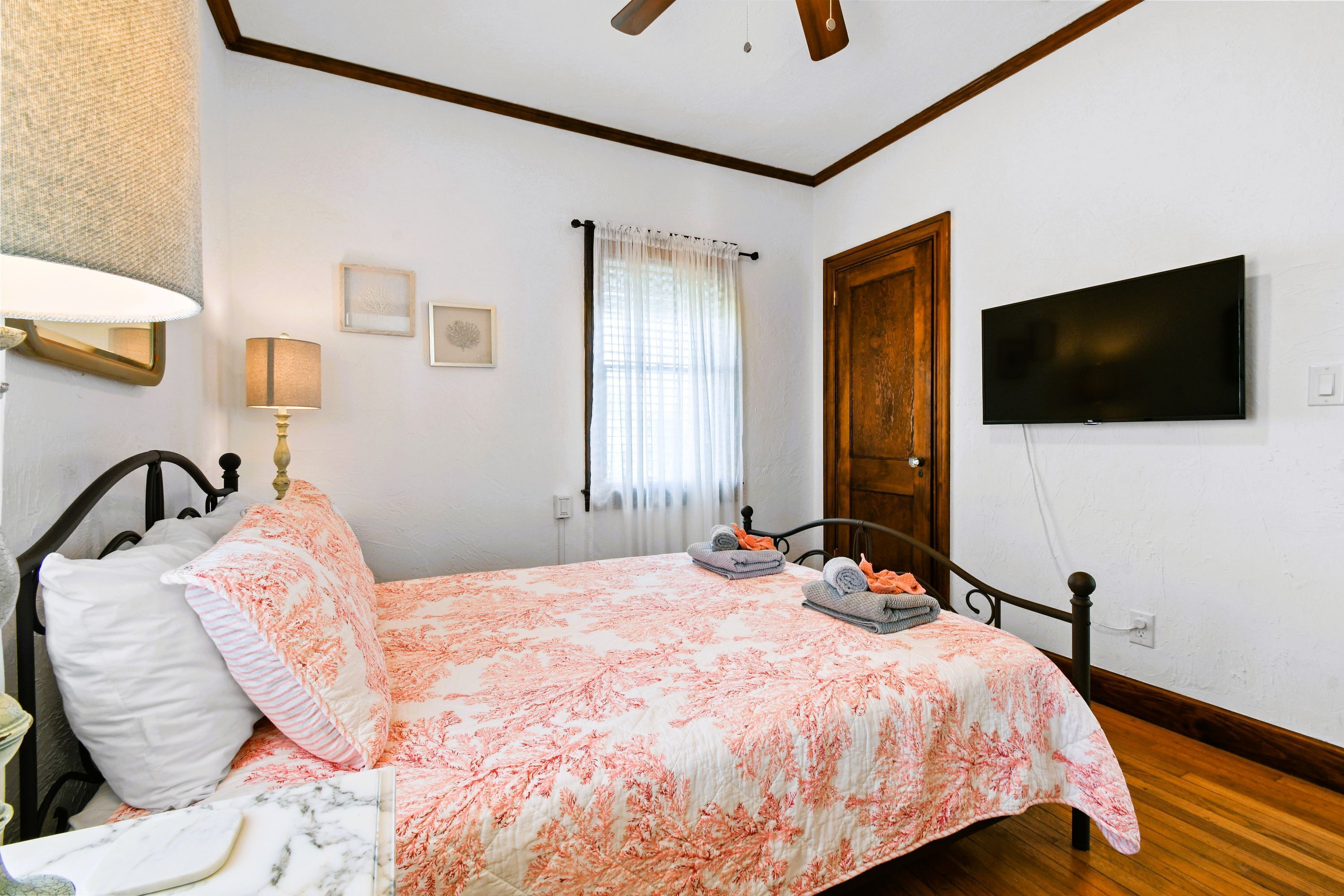 Une chambre à coucher avec un lit, une télévision, une fenêtre avec des rideaux et une porte en bois.