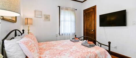 Une chambre à coucher avec un lit, une télévision, une fenêtre avec des rideaux et une porte en bois.
