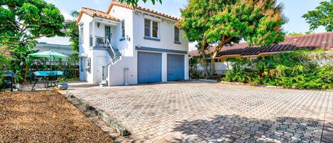 Une maison à deux étages, avec un toit en tuiles, un patio couvert aménagé avec du mobilier d’extérieur et une allée menant à un garage.