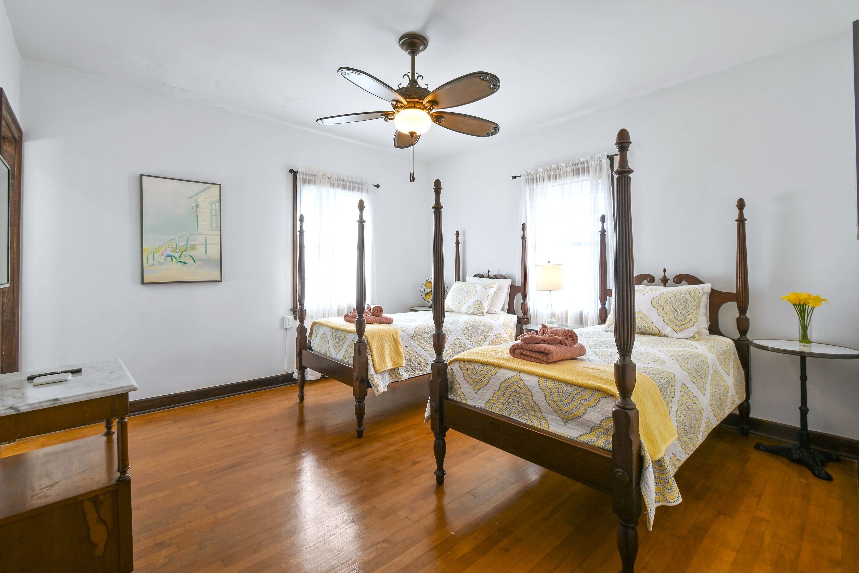A four-poster bed with a ceiling fan, wooden flooring, and a bedside table with a lamp.
