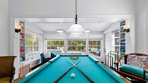 Een pooltafel met een wit plafond, houten stoelen en uitzicht op een zwembad.