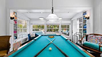 A pool table with a white ceiling, wooden chairs, and a view of a pool outside.
