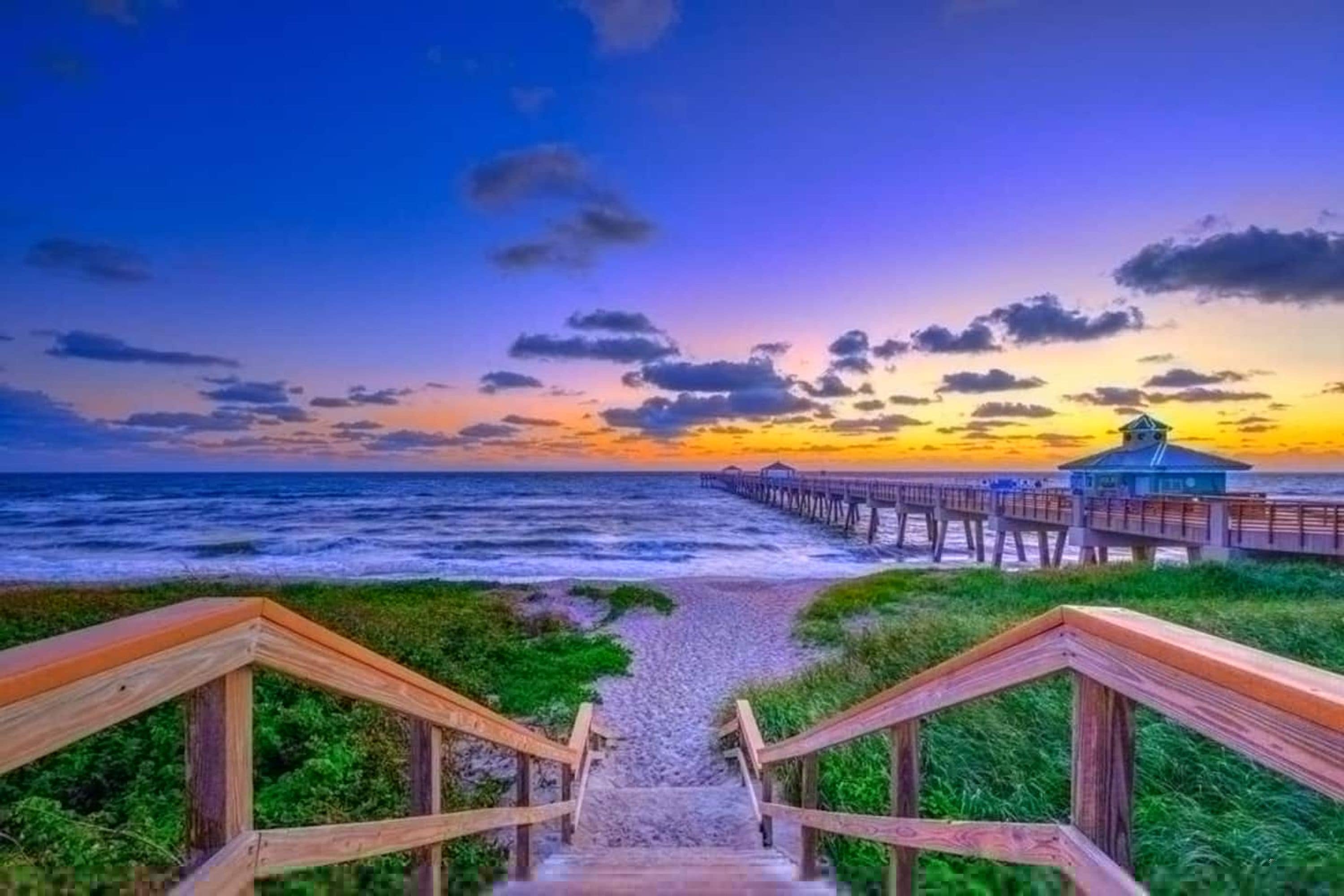 Una escalera de madera que lleva a una playa con un muelle y un pabellón.