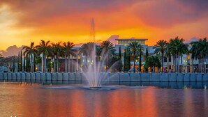 Hotel aan het water met een fontein, palmbomen en een zonsondergang.