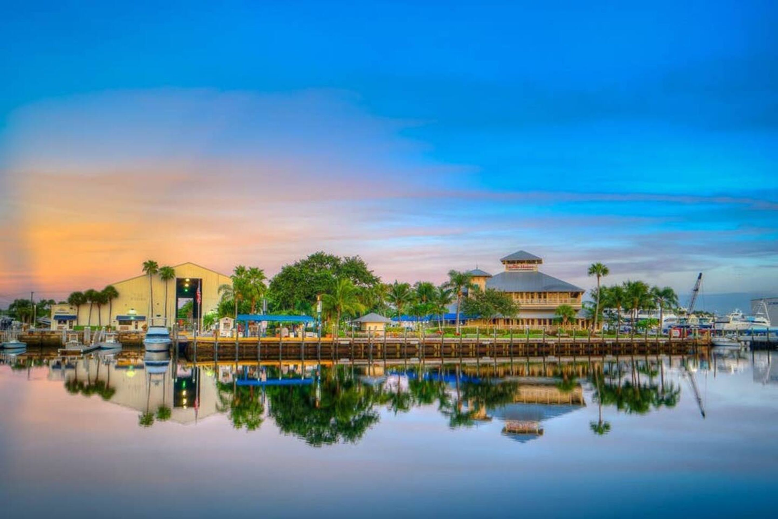 A waterfront hotel with a reflection in calm water, featuring a large building with a dome and a smaller structure with a sloped roof.