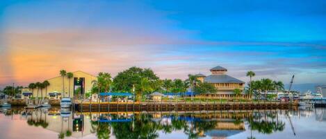 A waterfront hotel with a reflection in calm water, featuring a large building with a dome and a smaller structure with a sloped roof.