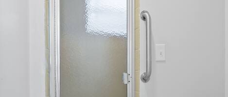 A bathroom with a glass shower door, a toilet, and a handrail.