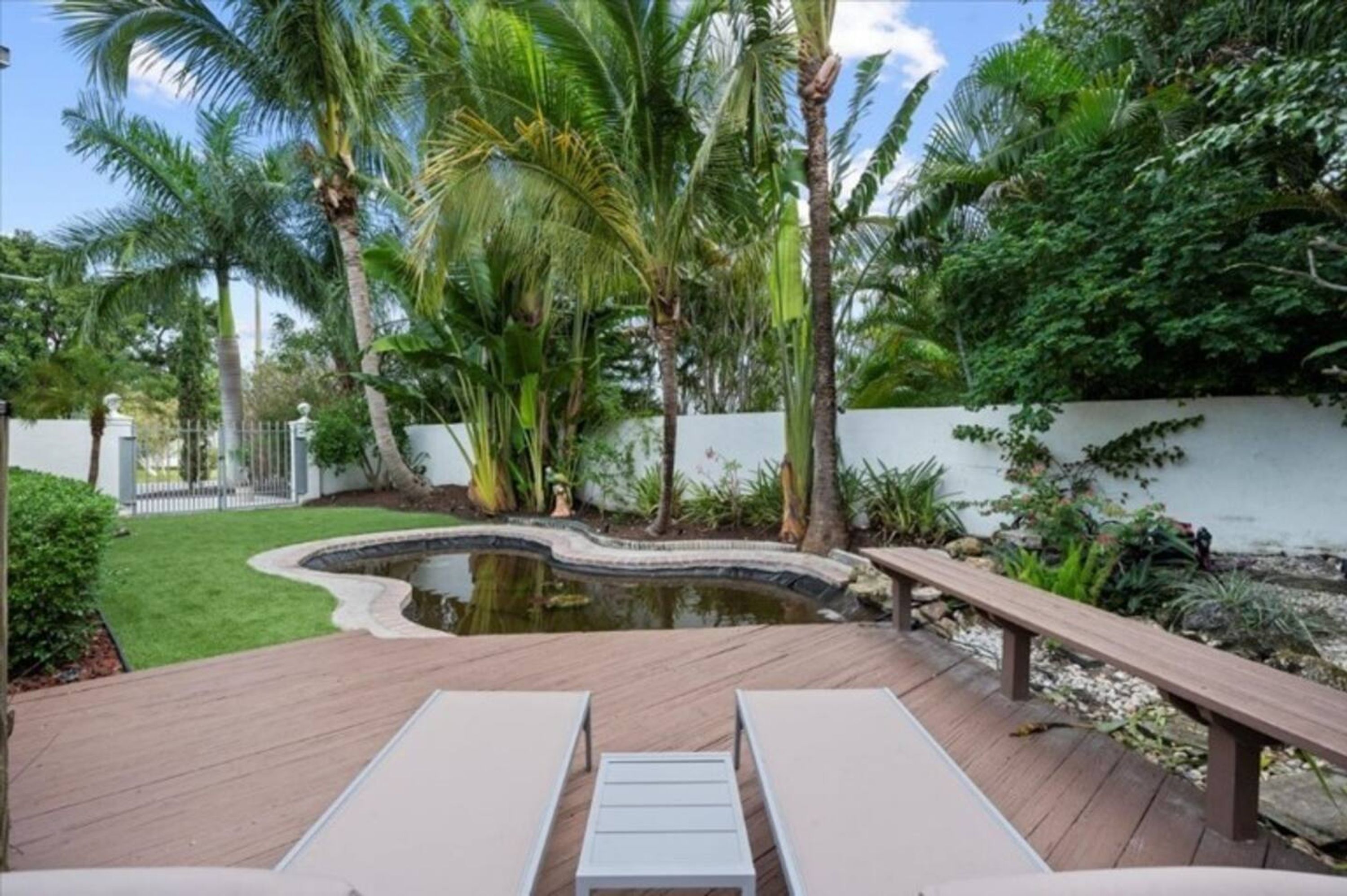 Una terraza de madera con dos sillones, un pequeño estanque y exuberante vegetación tropical.
