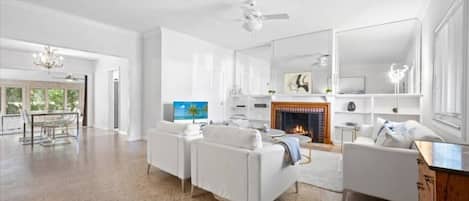 A spacious living room with white sofas, a fireplace, and a large mirror.