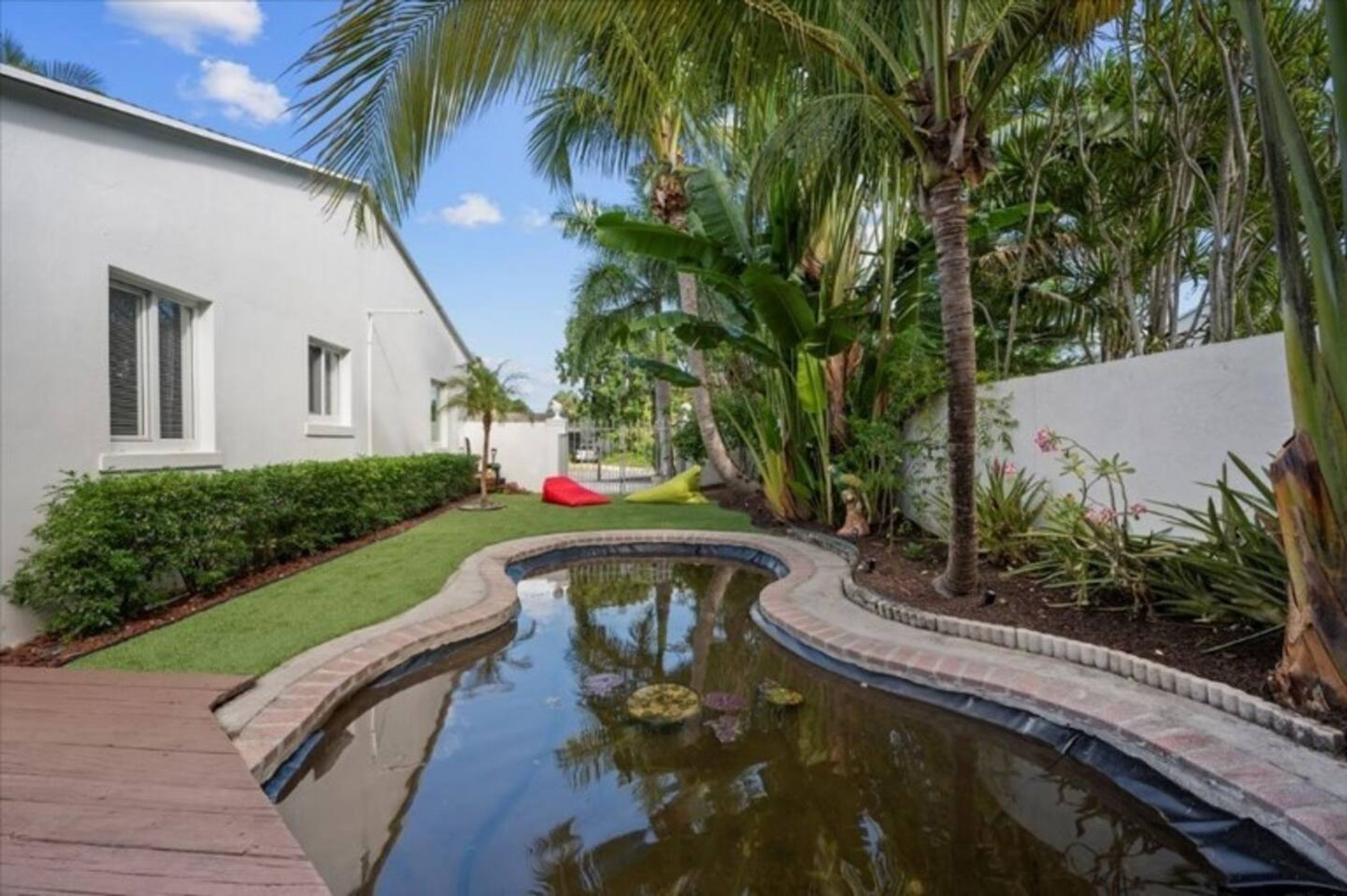 Una casa moderna con un pequeño estanque, palmeras y un césped bien cuidado.