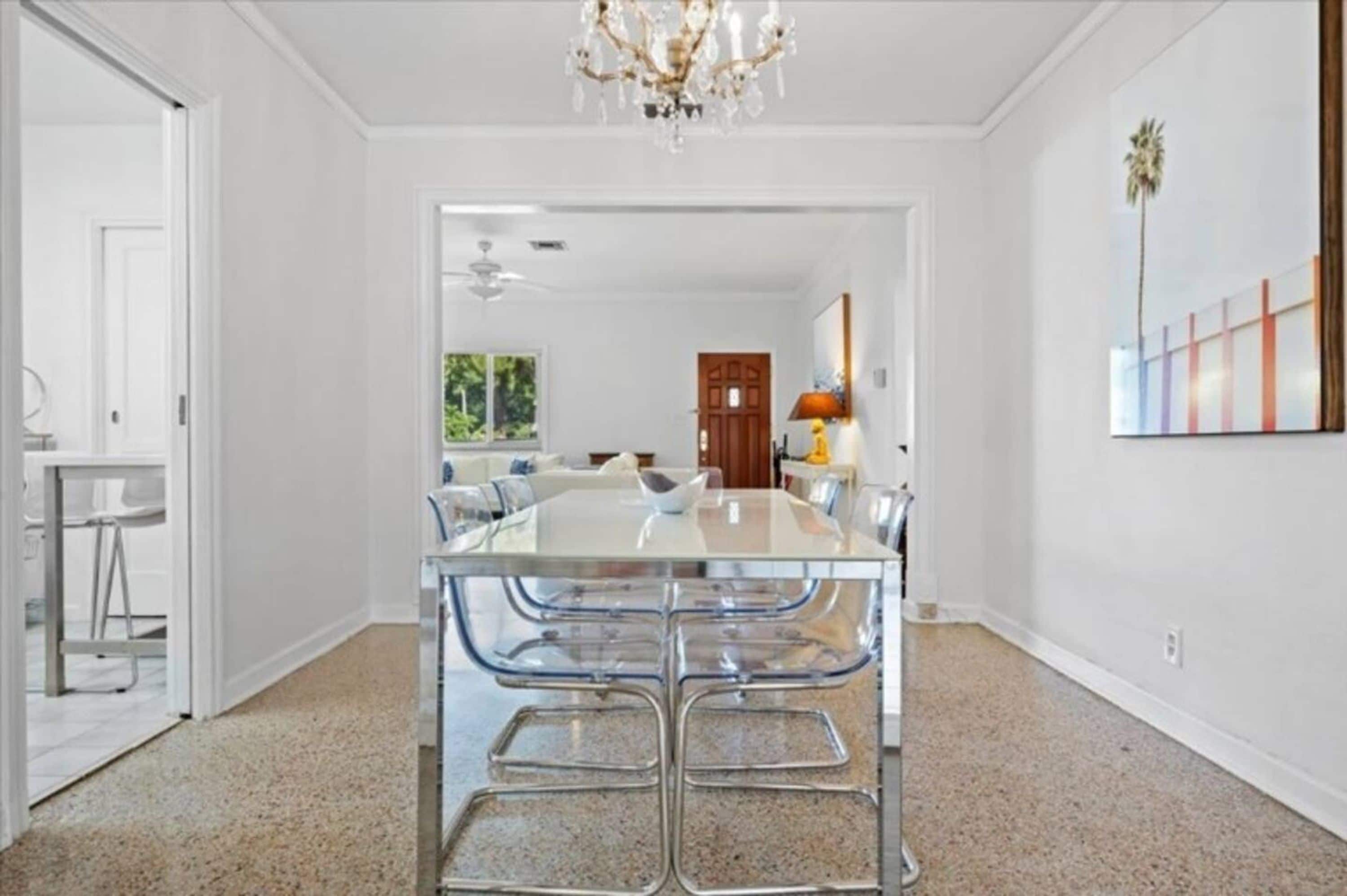 A modern kitchen with a glass dining table and metal chairs, a chandelier, and a view of the outdoors.