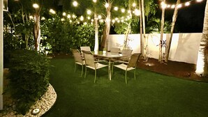 Eine Terrasse im Freien mit Tisch und Stühlen, umgeben von Pflanzen und Lichterketten.