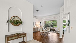 Uma sala de estar ampla com piso de madeira, uma mesa de jantar com cadeiras e uma grande janela com vista para o verde lá fora.