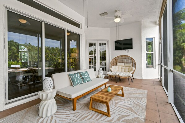 A spacious living area with a white sofa, wooden coffee table, and a wicker chair. - Why Is Everyone Obsessed With This House (Loxahatchee)