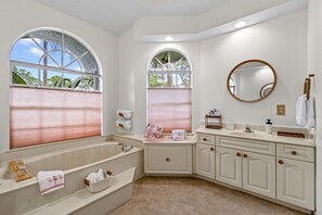 A bathroom with a large bathtub, a sink, a mirror, and two windows with blinds. - Why Is Everyone Obsessed With This House (Loxahatchee)