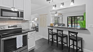 Una cucina moderna con mobili bianchi, forno a microonde integrato, piano cottura e una zona bar con due sgabelli.