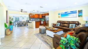 A spacious living room with a brown leather sofa, a coffee table, and a dining area with a kitchen in the background. - NEW Home w Guest Suite Pool Near PGA Beach (Palm Beach Gardens)
