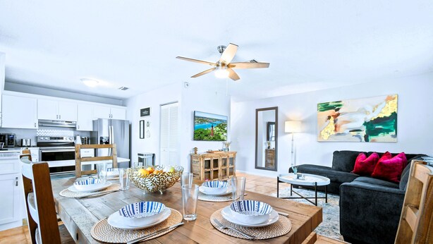 A modern kitchen with white cabinets, a dining table set for four, and a black sofa in the living area. - Luxury Sleeps 12 Kings Pool 2 Hot Tubs (Palm Beach Gardens)