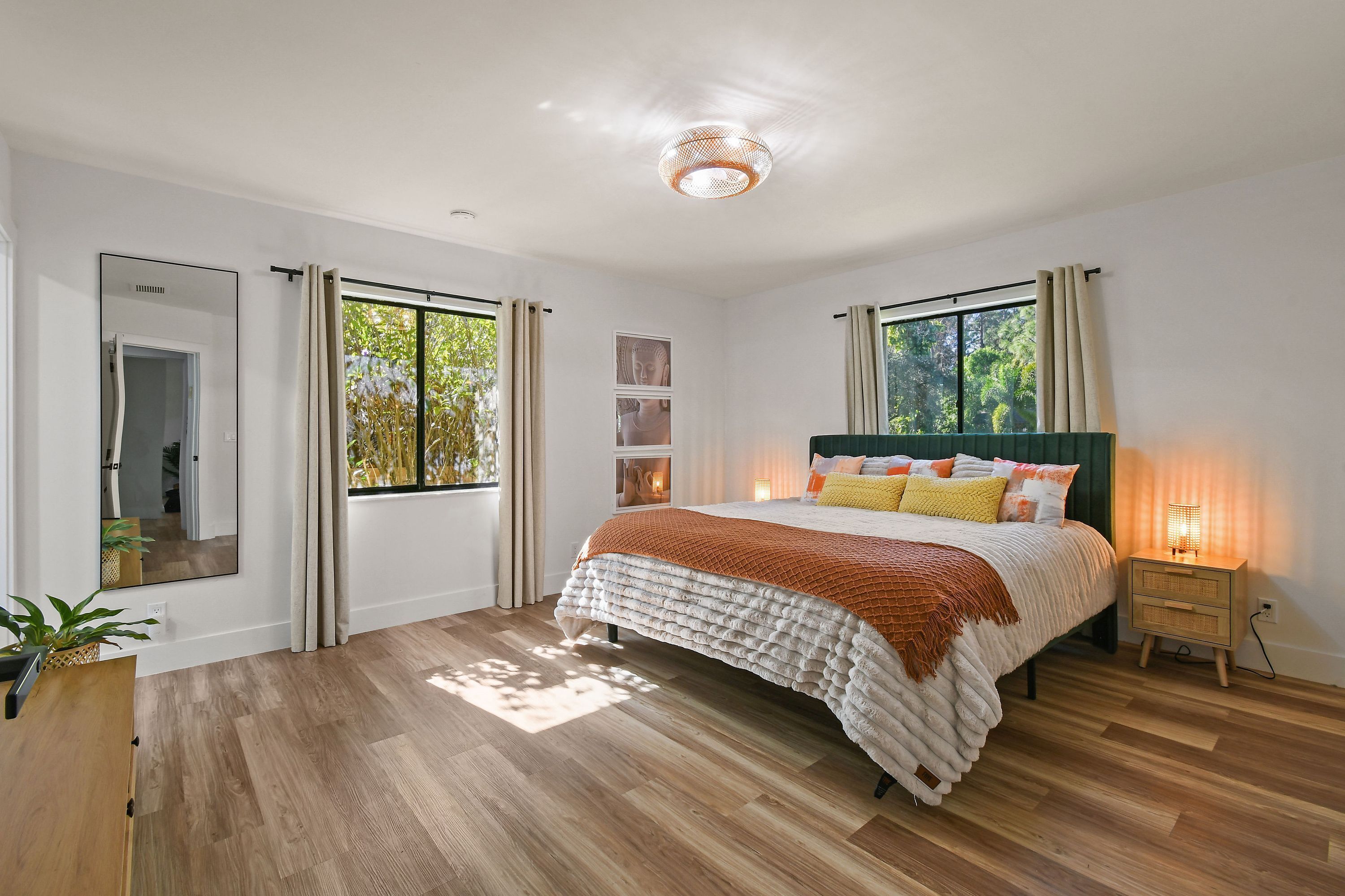 Un dormitorio con cama, mesitas de noche, un espejo y una ventana con cortinas.