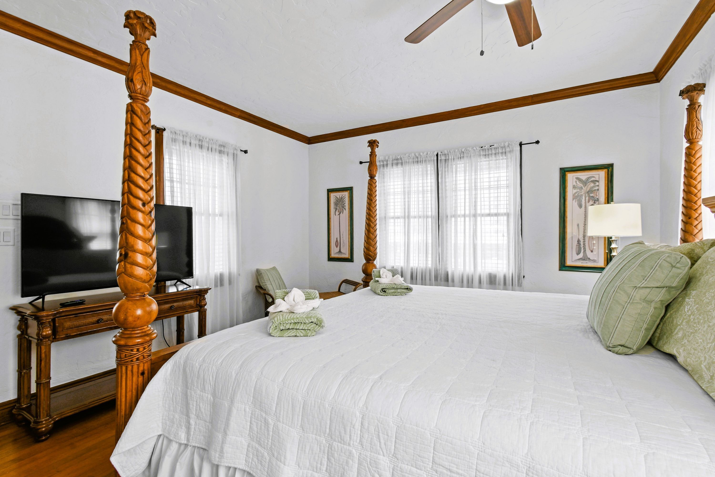 A large bed with a wooden headboard, a flat-screen TV, and a bedside table with a lamp.