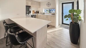 A modern kitchen with a large island, black bar stools, and a potted plant.
