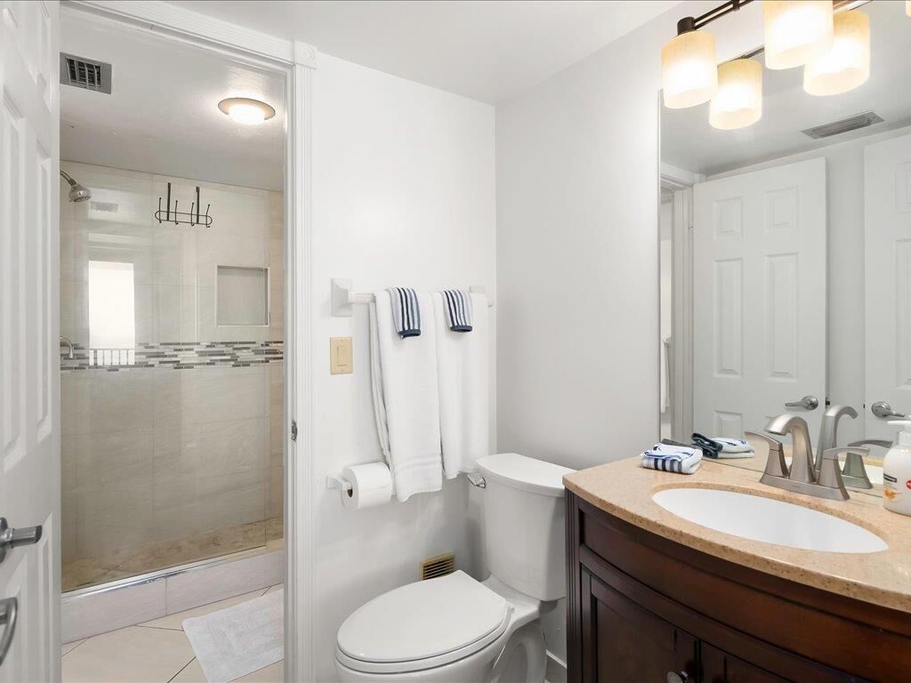 A bathroom with a glass shower enclosure, a toilet, a sink, and a mirror.