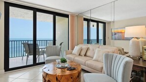 A modern living room with a sofa, armchair, and round coffee table. Large glass doors lead to a balcony with a view of the ocean. - Beachfront 2BR condo in Marco Island with pool and WiFi. (Marco Island)
