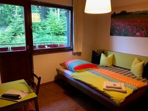 A bedroom with a bed, a desk, a chair, a window with a view of trees, and a painting on the wall. - Apartment '5' with Shared Terrace, Balcony and Wi-Fi (Dachsberg (Südschwarzwald))