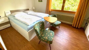A room with a bed, a small table, two chairs, a window with curtains, and a radiator. - Apartment '5' with Shared Terrace, Balcony and Wi-Fi (Dachsberg (Südschwarzwald))