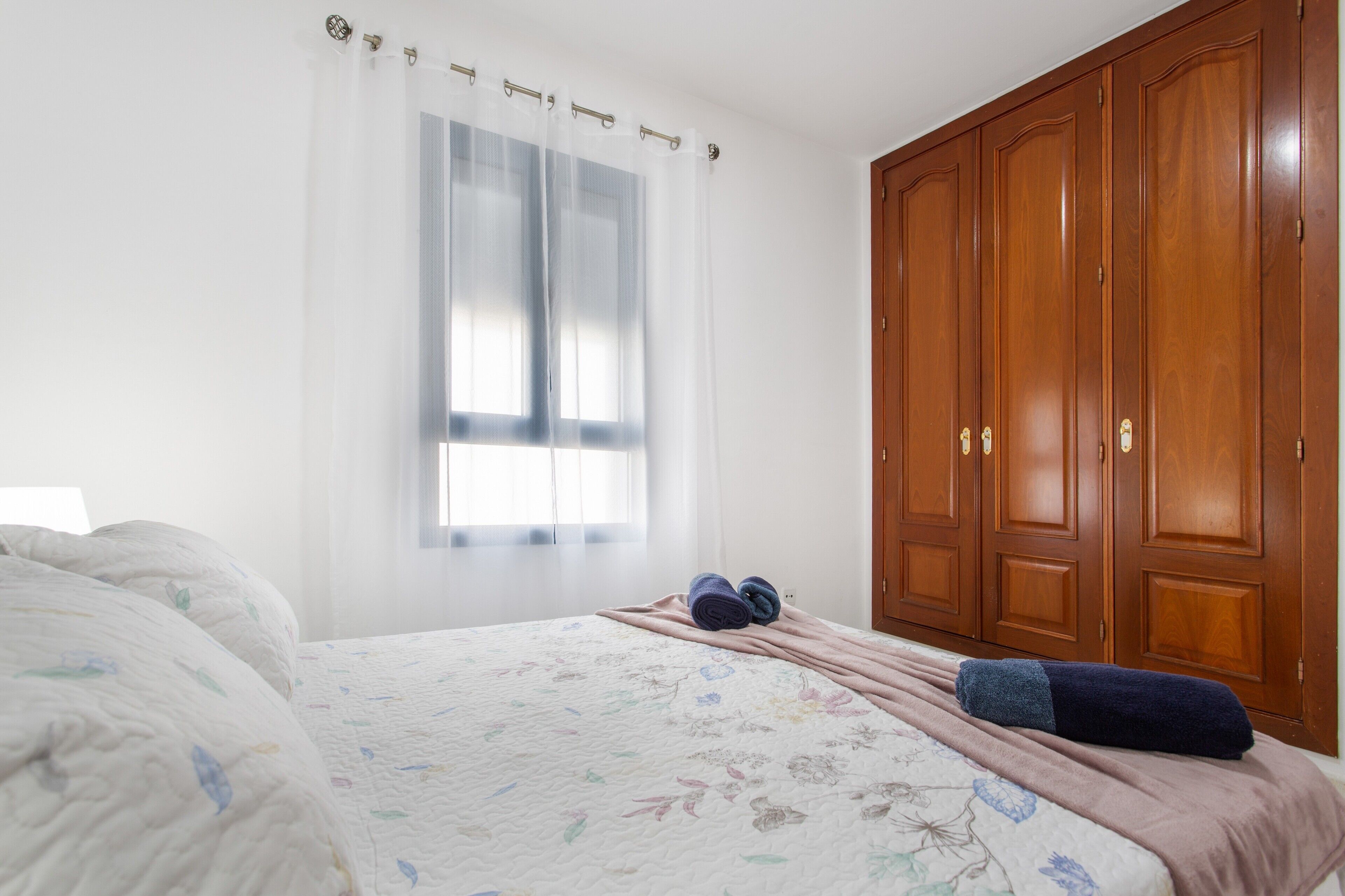 A bedroom with a bed, a window with curtains, a wardrobe, and a blanket on the bed.