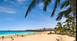 A beach with palm trees, a clear blue sky, and a building in the background.