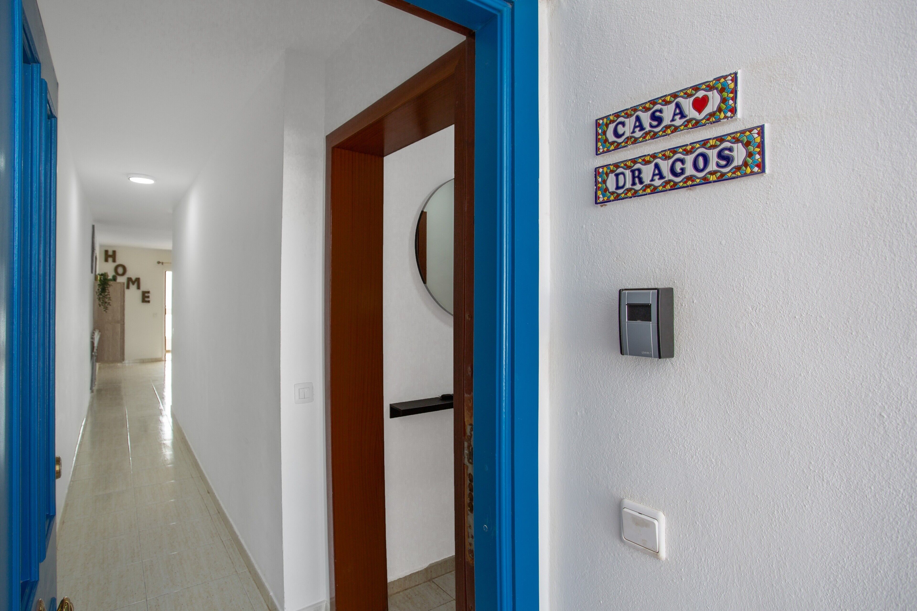 A hallway with a blue door frame, a wall-mounted light switch, and two decorative signs reading 'CASA DRAGOS'.