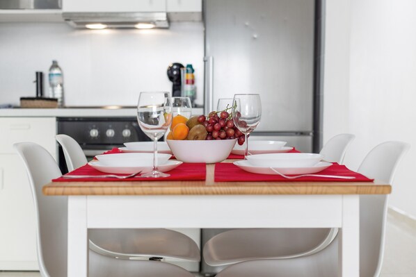 A modern kitchen with a dining table set for two, featuring a bowl of fruit and wine glasses.