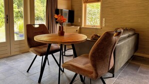 A modern dining area with a round table, two chairs, a vase with flowers, a sofa, and a television. - Chalet with privacy and garden near Leeuwarden (Jelsum)