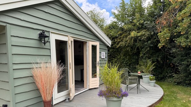 A house with a wooden deck, a sliding glass door, and a patio area with outdoor furniture. - Chalet with privacy and garden near Leeuwarden (Jelsum)