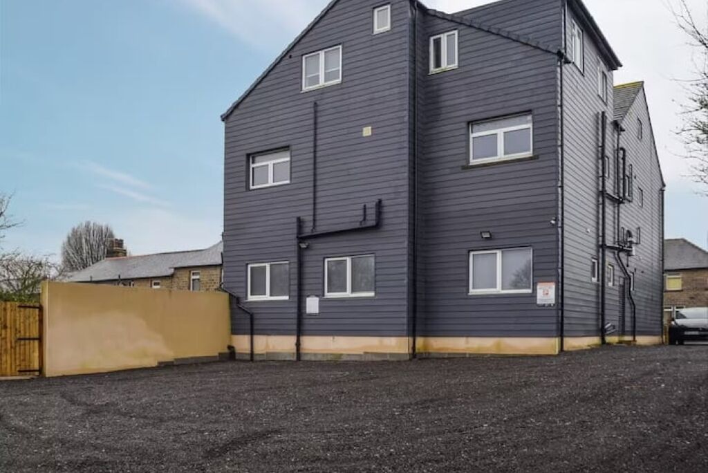 A multi-story building with a dark exterior, a gated driveway, and a gravel parking area.