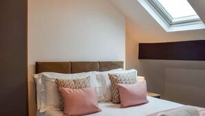 A neatly made bed with a headboard, pillows, and a rolled towel. - Elysian Residence (Newsome)