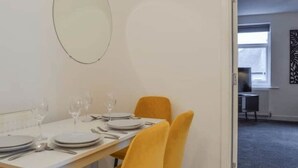 A dining area with a white table set for four, two yellow chairs, and a large oval mirror on the wall. - The Nivora Suite (Newsome)