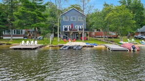 A lakeside cabin with a dock, chairs, and kayaks.