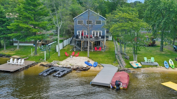 Un chalet au bord du lac, avec un quai, des kayaks et un espace salon extérieur.