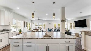 A spacious kitchen with white cabinetry, granite countertops, pendant lighting, and a large island.