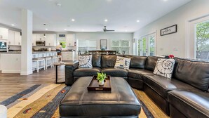 A modern living room with a sectional sofa, a coffee table with a plant, and a kitchen in the background.