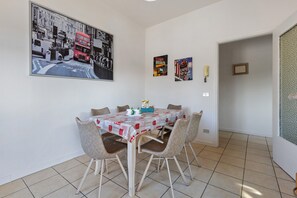 Un comedor con una mesa dispuesta para cuatro, sillas, un cuadro enmarcado en la pared y una puerta que da a otra habitación.