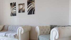 Dos sofás blancos tapizados con detalles capitonados, ubicados en un rincón de una habitación con suelo de baldosas.