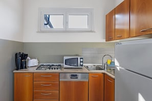 Una cocina compacta con armarios de madera, un microondas, una estufa a gas y un lavavajillas.