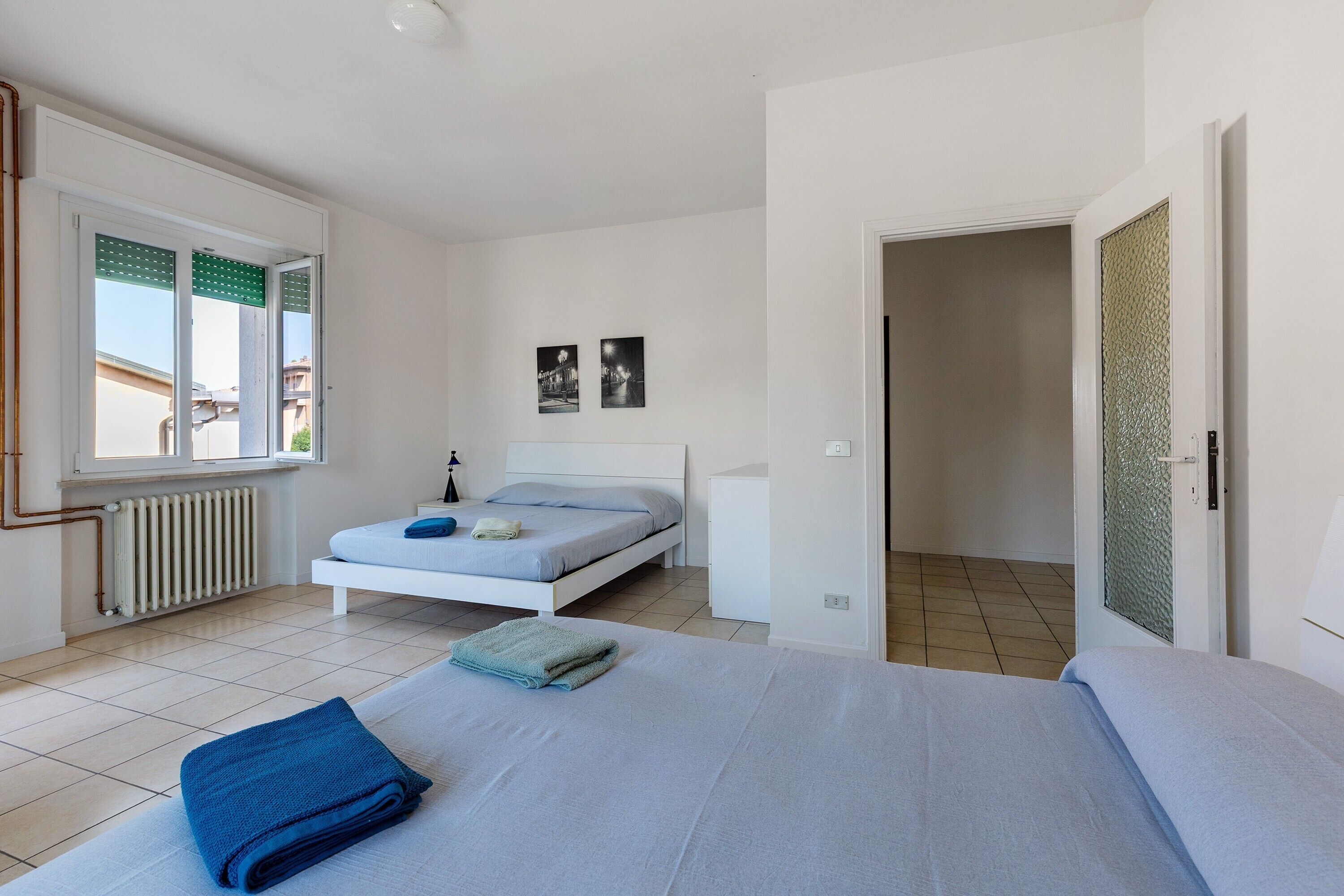 Une chambre à coucher avec un lit, une fenêtre, un radiateur et une porte donnant sur une autre pièce.