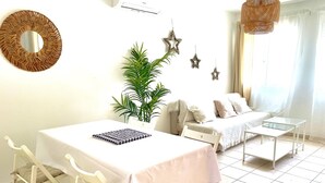 A well-lit room with a dining table, a sofa, a small coffee table, and a potted plant.