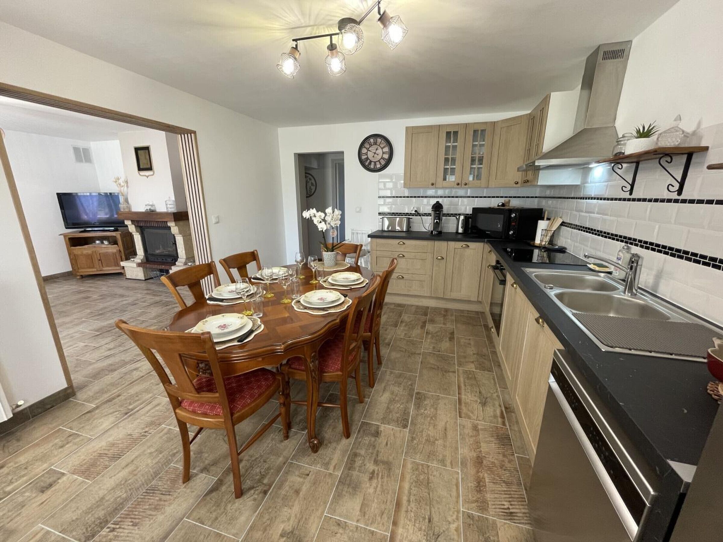 Une cuisine moderne avec des meubles en bois, un plan de travail noir et un coin repas comprenant une table et des chaises en bois.