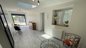 A spacious room with a high ceiling, a dining area with a table and chairs, a seating area with a round metal table, and a window with a view of the outdoors. - Peaceful cottage with garden in Savonnières (Savonnières)